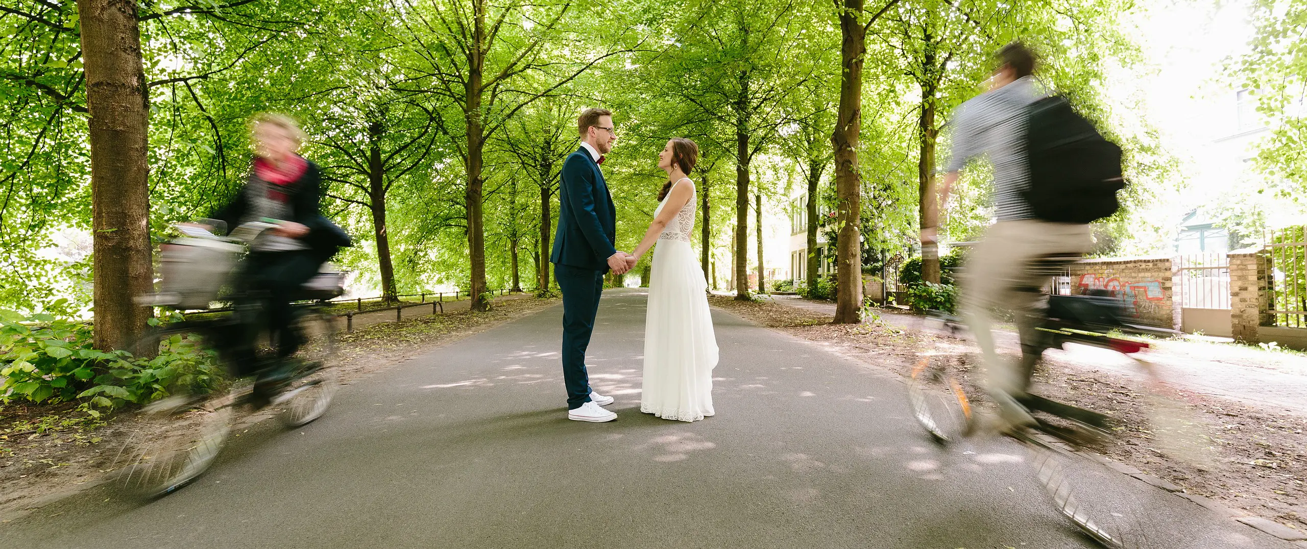 Hochzeitspaar mit zwei Fahrradfahrern auf der Promenade in Münster mit dem Hochzeitsfotograf Münster