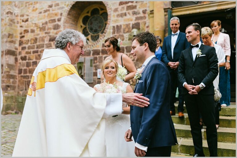 Brautpaar nimmt die Glückwünsche vom Pastor vor der Kirche entgegen ©Hochzeitsfotograf Bad Iburg