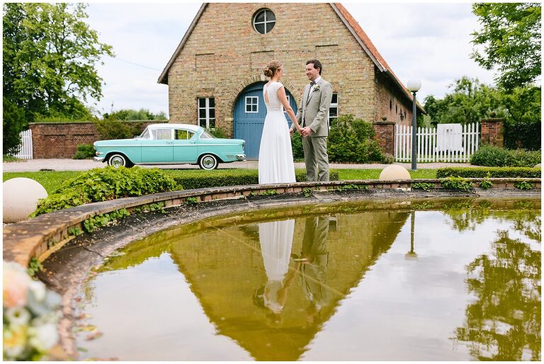 Brautpaar vor dem Brunnen mit Brautauto im Hintergrund ©Markus Koslowski Hochzeitsfotograf Haus Venne